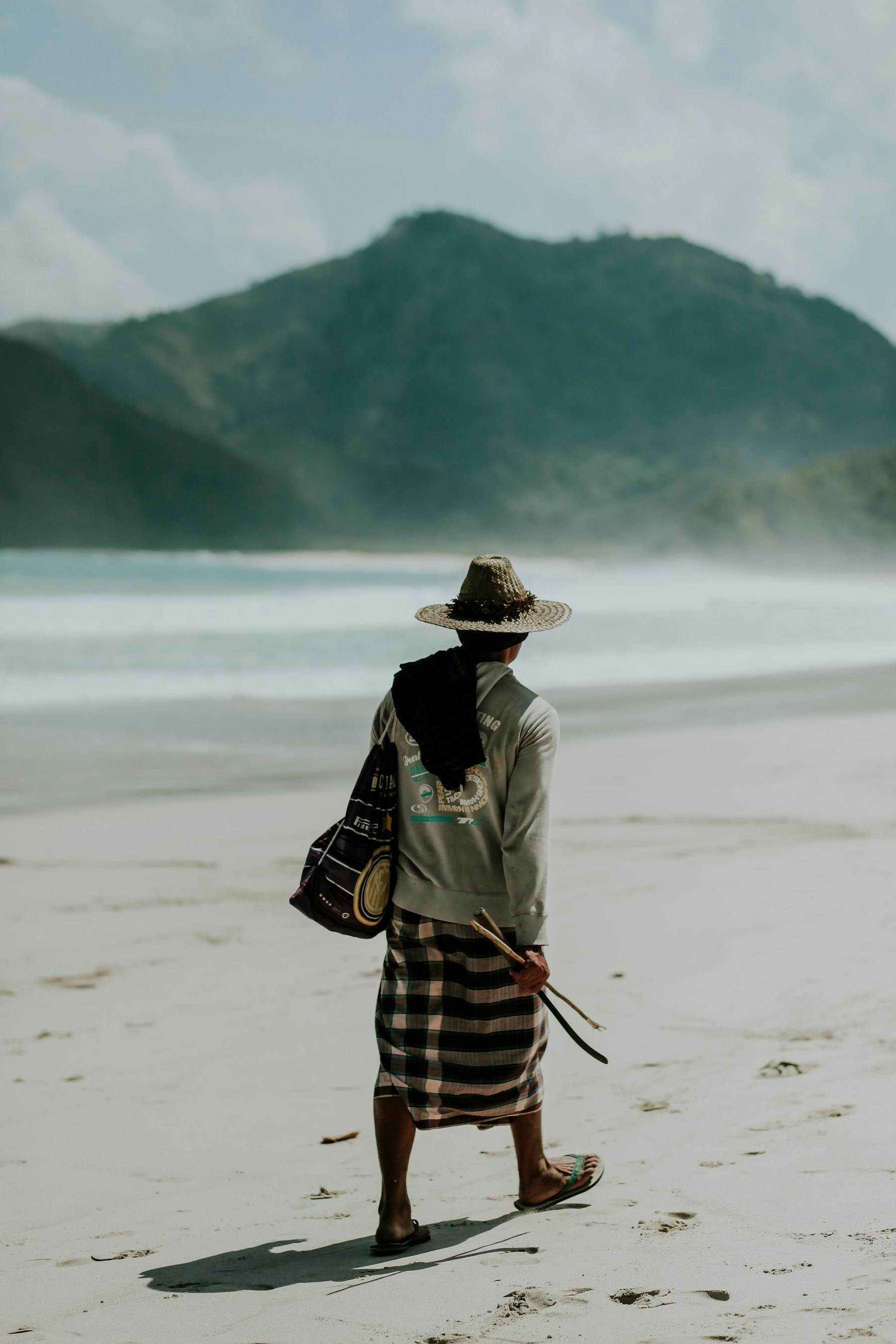 Local walking along a white-sand beach in South Lombok, mountains behind